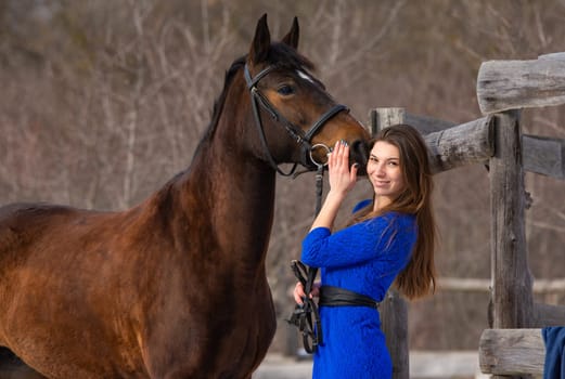 A beautiful girl with a horse is standing near an old wooden fence