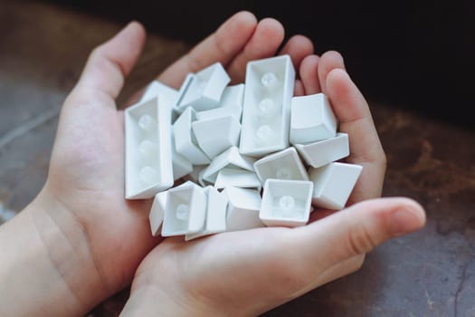 top view closeup of Caucasian child hands holding many pbt keycaps of a white mechanical keyboard in natural lighting