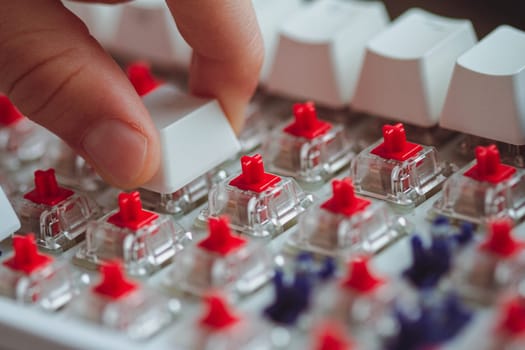 perspective view closeup of child fingers switching a custom keycap on a white mechanical gaming keyboard with red cherry switches