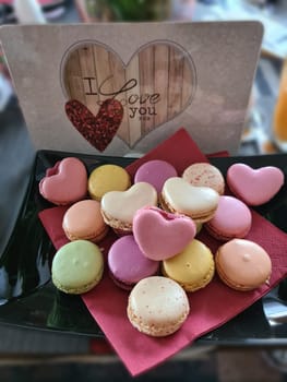 Top view of three delicious macarons and love heart symbol on napkin on wooden table. Romantic vintage valentines day and wedding background