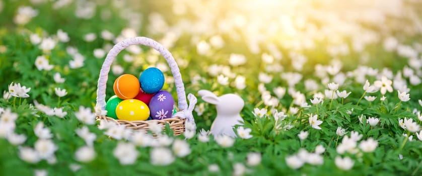 Panoramic view of the spring field with rabbit toy and bascket with colourful eggs on it. Concept of the Easter holiday.