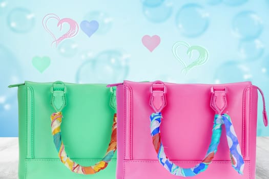 Happy Valentines or Mothers Day template. A beautiful green and a pink women's handbag decorated with a colourful cloth on the table over abstract blue heart background.