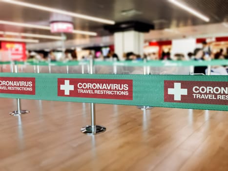Green ribbon barrier inside an airport with the warning of travel restrictions due to the worlwide spread of Coronavirus