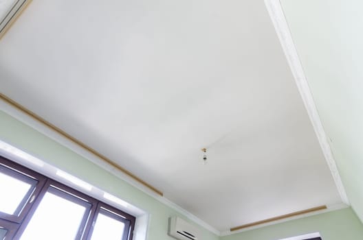 Plastered white ceiling in the room, a temporary light bulb hangs on the ceiling