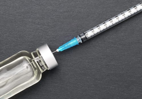 Liquid medicine in vials and injection syringe on dark gray background