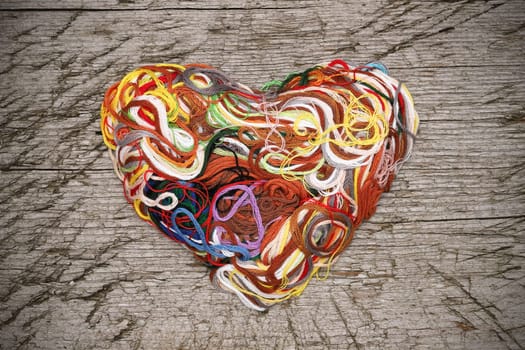 Heart shaped entangled thread on grungy wooden background