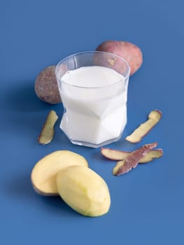 A transparent glass with vegetable potato milk on blue table near to potato tubers. Vegan plant based lactose free Milk close up. Healthy eating and Alternative food concept.