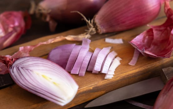 Sliced Red tropea onions with a knife on a wooden board close up. Traditional local south italian vegetable. Cooking process in home kitchen