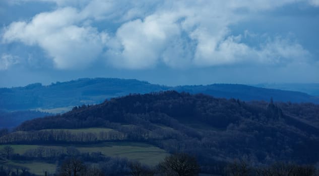 Blue landscape with hill and forest and cloudy sky