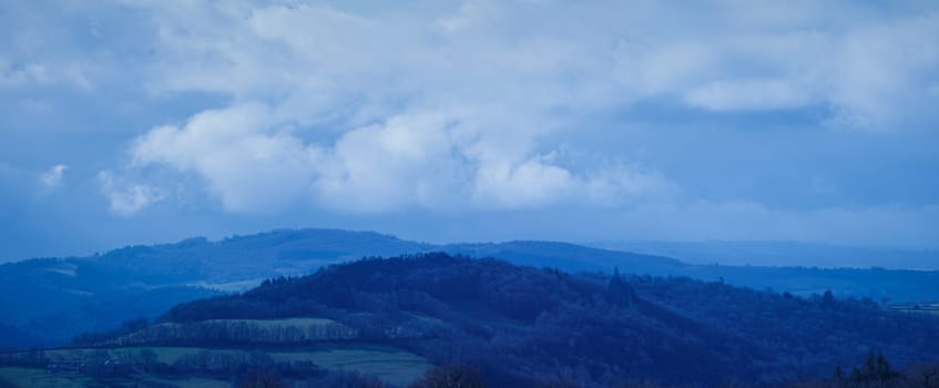 Blue landscape with hill and forest and cloudy sky