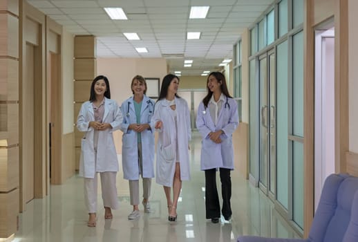 One mature doctor and three young females doctor walking and discussing diagnosis in hospital corridor. Teamwork and healthcare concept
