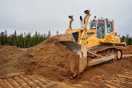 A yellow tractor levels the site with sand. High quality photo