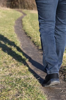 Go new ways. A woman is hiking in a park along a dirt trail in autumn or spring.