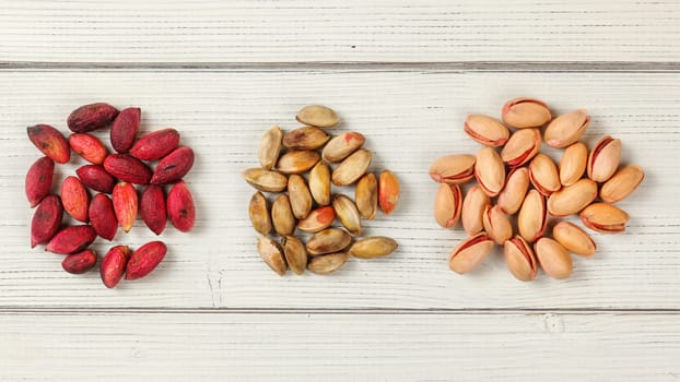 Red Turkish pistachios on white boards. Partly dried dark pink fruits, when peeled, nuts are inside, and finally, roasted pistachio. Tabletop view.