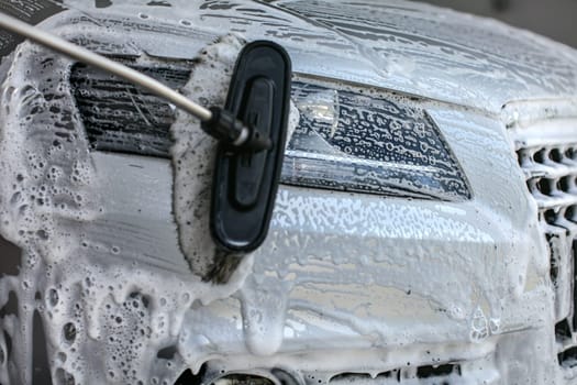 Front light of silver car washed in self service carwash. Brush leaving strokes in shampoo and foam