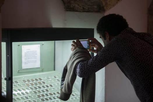 Osuna, Spain - April 20th, 2019: Visitor taking pictures to ancient coins glass cabinet. Osuna Archaeological Museum, Seville