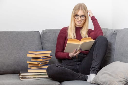 Young woman is sitting on the couch holding a open book and smiling at the camera. Self education concept.