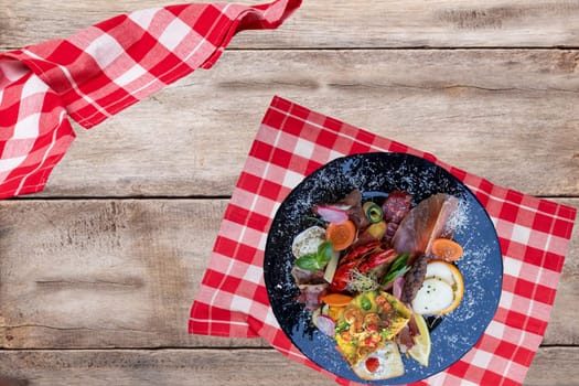 Traditional italien food. Closeup of mixed mediterranean appetizers or antipasto and tapas with ham vegetables and cancer on a black plate on a rustic wooden table. Top view.