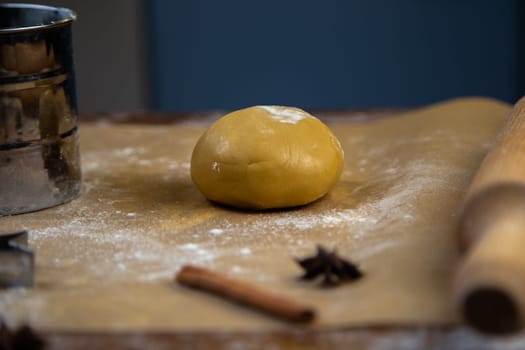 There is a dough on the parchment, a little sprinkled with flour, a rolling pin, cookie cutters, cinnamon and a metal flour jar are visible around. High quality photo