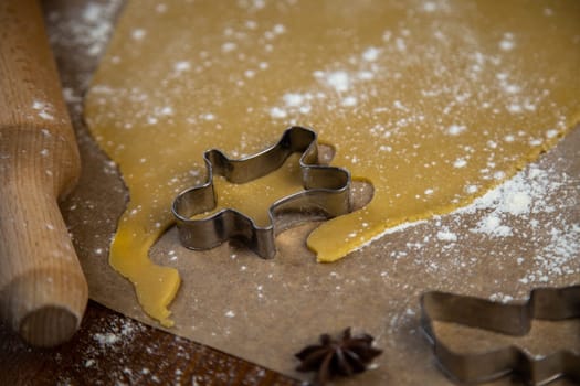 On the parchment there is a carver in the form of a man near the rolled dough, everything is sprinkled with flour, a rolling pin and other molds are visible, a photo in a dark key. High quality photo