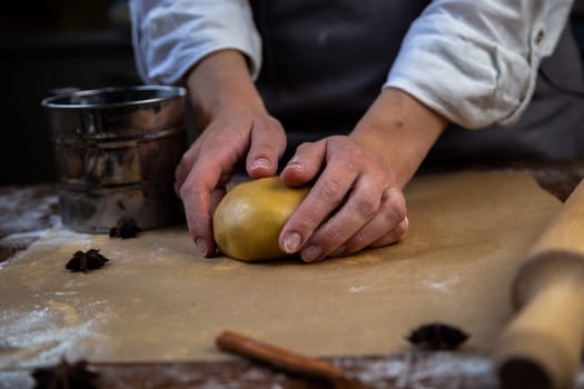 There is a dough on the parchment, slightly sprinkled with flour, which the cook holds in his hands, a rolling pin, cookie cutters, cinnamon and a metal flour jar are visible around. High quality photo