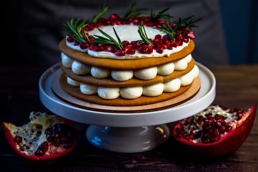 A cake of three layers, consisting of cakes and white cream, decorated with pomegranate and rosemary on top, stands on a white stand sideways on a dark background. High quality photo
