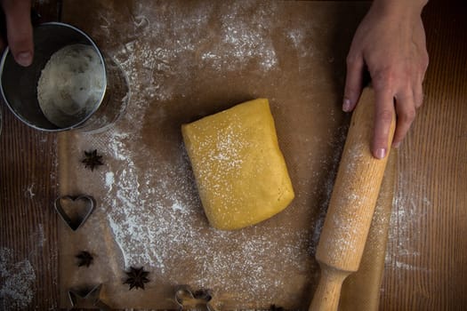 A rectangle of dough lies on baking parchment, a rolling pin and cookie cutters are lying next to it, everything is strewn with flour, a cook is standing in the background and holding a rolling pin and flour powder. High quality photo