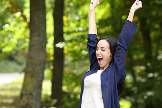 Excited woman in a park raising arms celebrating success