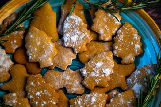 Cookies in the form of Christmas trees lie on a blue plate, decorated with rosemary on the sides on a dark background. High quality photo