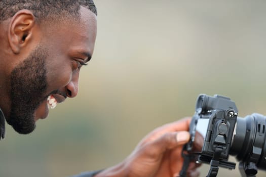 Photographer with black skin checking photos on mirrorless camera screen outdoors