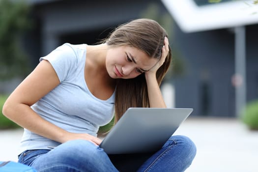Sad teenage female checking laptop complaining alone in the street
