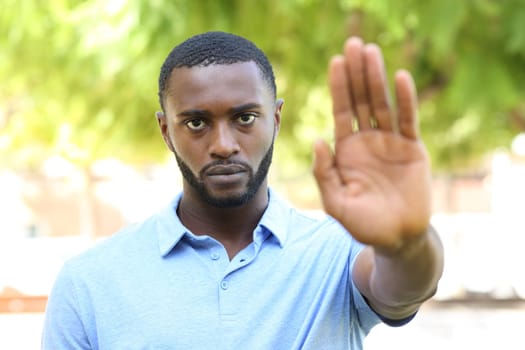 Front view portrait of an angry black man gesturing stop sign in a park