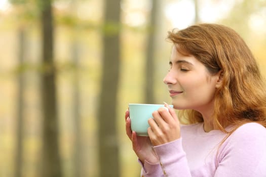 Profile of a woman drinking coffee in a forest in autumn