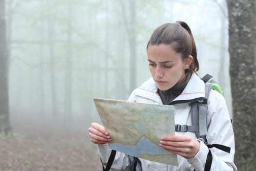 Serious trekker checking paper map to find location in a forest