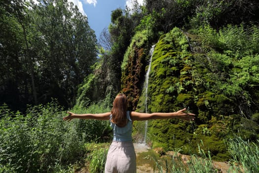 Back view portrait of a woman outstretching arms celebrating in a little water fall