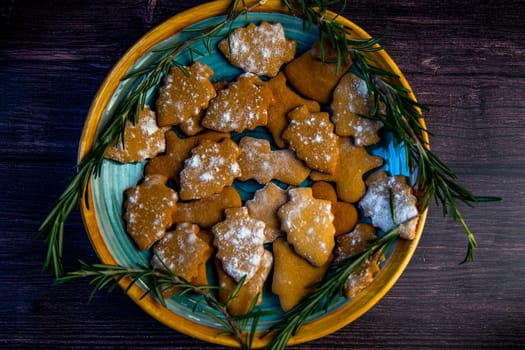 Cookies in the form of Christmas trees lie on a blue plate, decorated with rosemary on the sides on a dark background. High quality photo