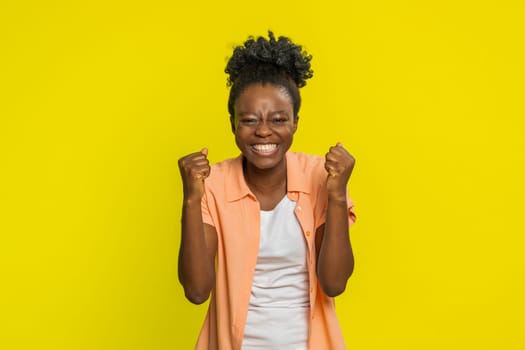 Happy joyful African American woman celebrating success victory, winning birthday lottery jackpot goal achievement play game good positive news triumph. Young Black girl isolated on yellow background