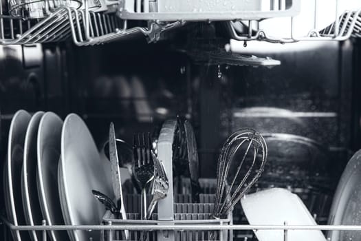 Front view of open automatic stainless steel built-in fully integrated top control dishwasher range machine with clean utensils, cutlery, glasses, dishes, plates inside in modern home kitchen