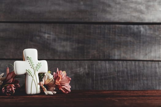 Easter holiday conceptual background on rustic wooden boards. Photo of white gingerbread cookie Cross shape, flowers bouquet on table top. Card with copy space to place text. Minimal concept