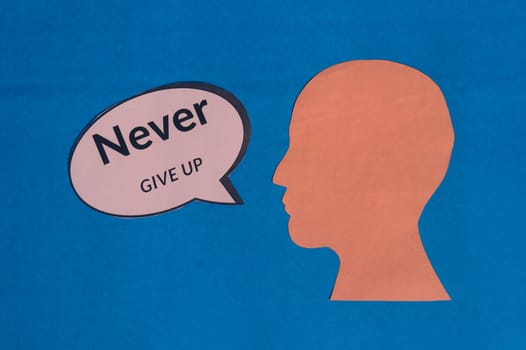 Paper human face with motivation text on speech bubble isolated on blue background. Conceptual image shows believing in yourself and willingness to accept failure to achieve goals