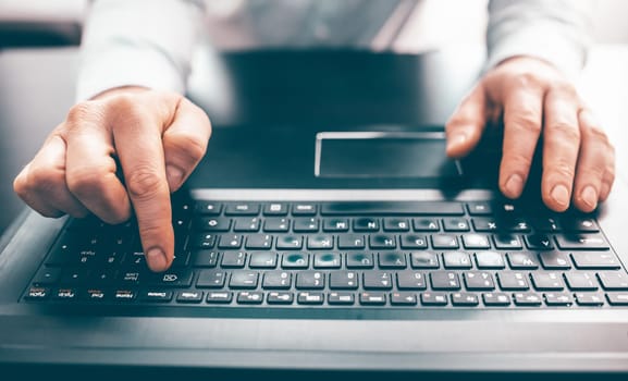 Close up of business man hand working on laptop computer on wooden desk as concept