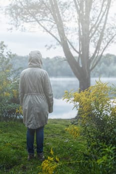 Back of a woman with depression standing alone at the lake pouring rain