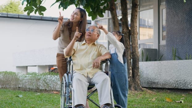 Disabled senior grandpa on wheelchair with grandchild and mother in park, Happy Asian three generation family having fun together outdoors backyard, Grandpa and little child smiling and laughed
