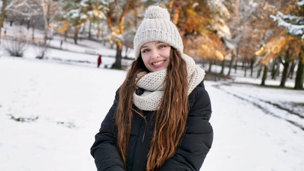 Young beautiful caucasian woman goulash in snowy winter park close up in slow motion. Happy girl with long brown hair enjoys winter and smiles on Christmas Eve and Happy New Year