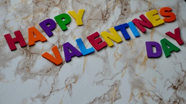 Happy Valentines Day LGBT, colored rainbow text, on marble background close up.