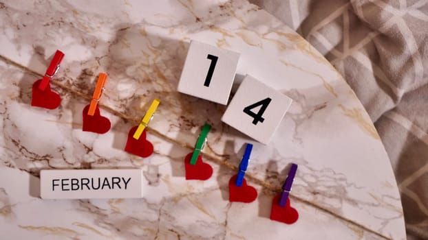 Happy Valentines Day LGBTQIA, colored rainbow clothespins with red hearts and text, on marble background close up.