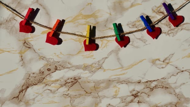 Happy Valentines Day LGBTQIA, colored rainbow clothespins with red hearts and text, on marble background close up.