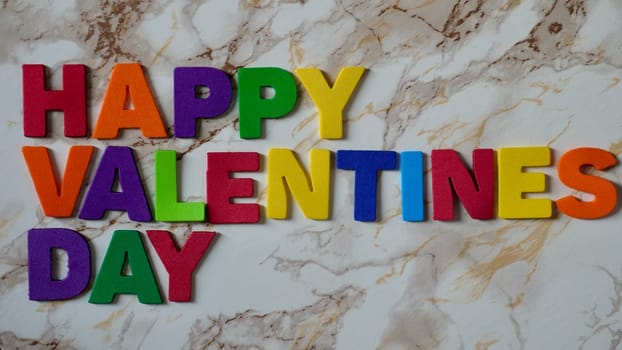 Happy Valentines Day LGBT, colored rainbow text, on marble background close up.