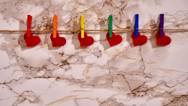 Happy Valentines Day LGBTQIA, colored rainbow clothespins with red hearts and text, on marble background close up.