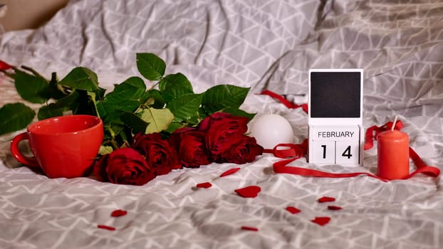Festive Flatlay, composition for Valentine's Day on February 14. Coffee in a red cup, red rose flowers and calendar at home in bed in spatial date